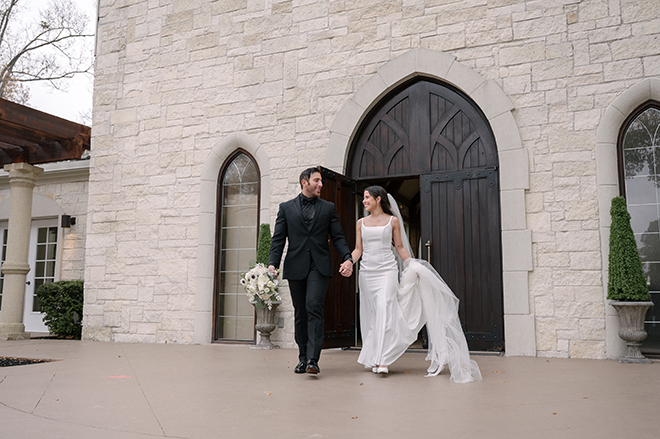 The bride and groom hold hands as they walk out the chapel. 