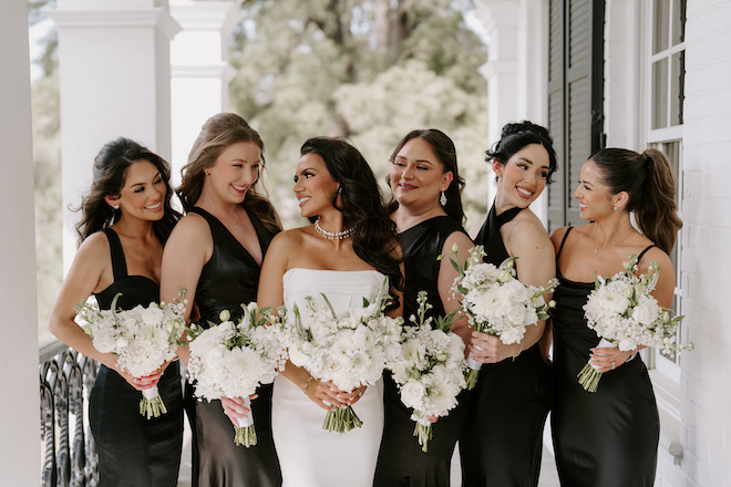 Bridesmaids all looking and smiling at the bride in their black dresses holding the white bouquets.