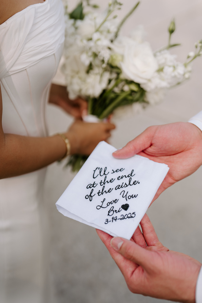 Close up of the groom holding a napkin from the bride that reads, "I'll see you at the end of the aisle. love you. Bri" with a heart.