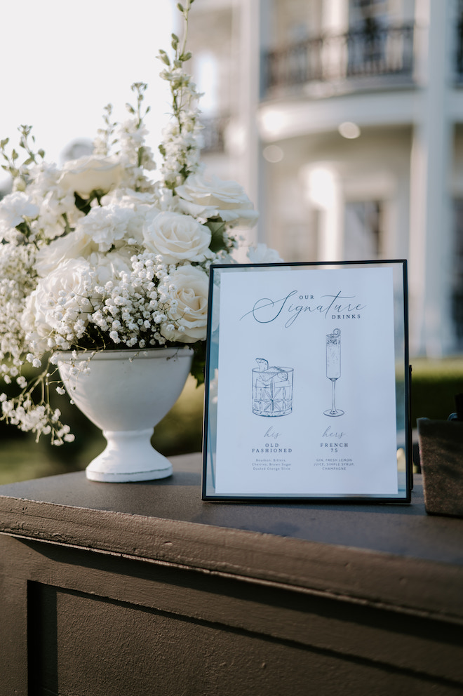 Signature drinks frame outside of the venue next to a white flower vase for cocktail hour "his and hers" his being an old fashioned and hers being a french 75