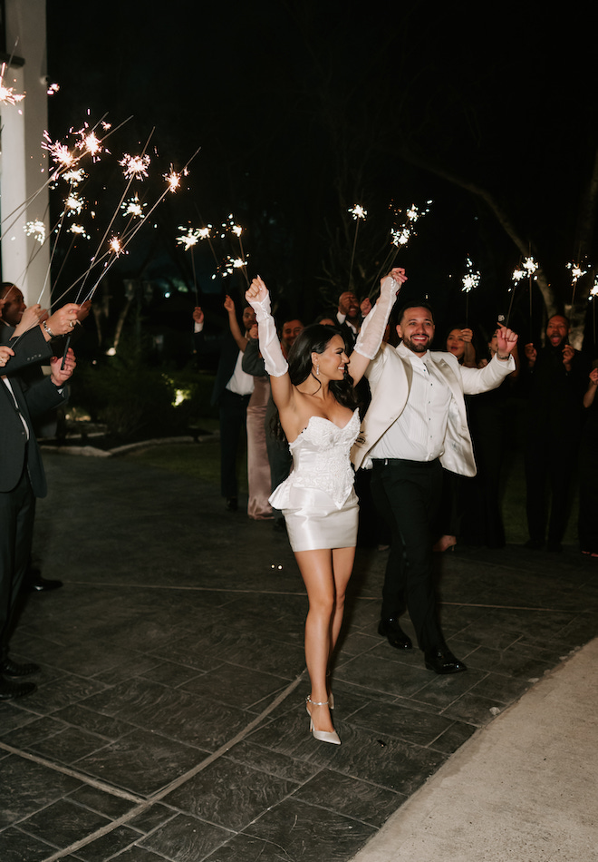 The bride, wearing her mom's wedding gown transformed into a modern mini, and groom exiting while guests hold sparklers around them