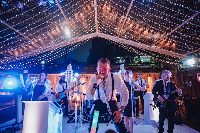 Danny Ray and the Atlantic Street Band perform under string lights at a tented wedding in Houston. 