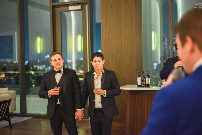 The grooms holding hands while listening to a speech. 