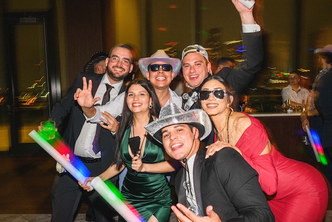The grooms wearing disco-inspired hats while posing for a picture with guests. 