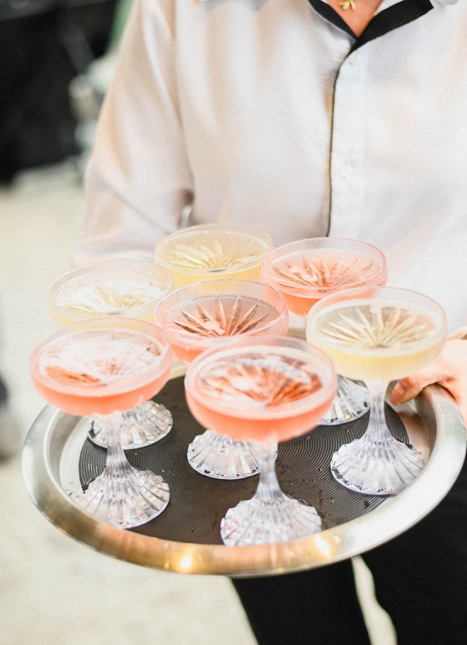A tray of champagne and rose drinks in coupe glasses. 
