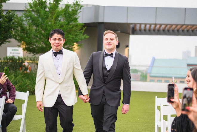 The grooms with tears in their eyes holding hands walking down the aisle at Thompson Houston, by Hyatt. 