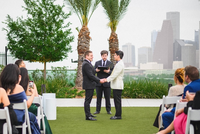 The grooms holding hands at the altar overlooking the skyline at Thompson Houston, by Hyatt. 