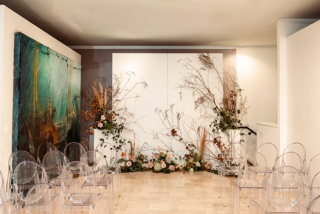 Floral arrangement on white risers are placed at the front of the altar for the wedding ceremony in the art gallery. 