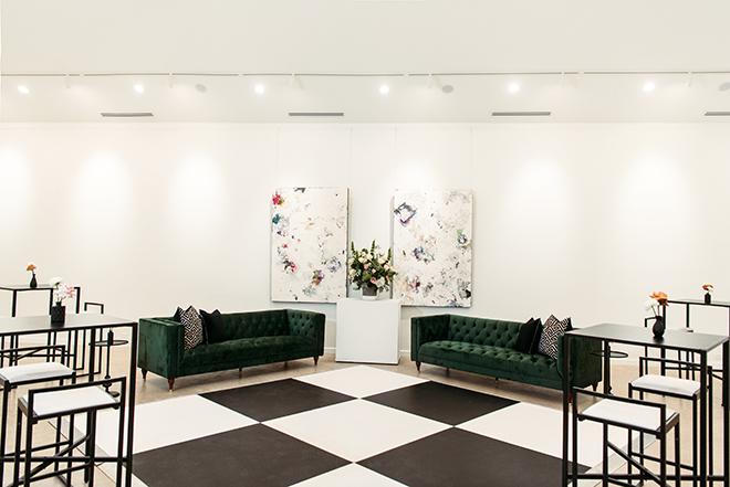 A black and white checkered dance floor is placed in the art gallery around emerald green lounge seating.