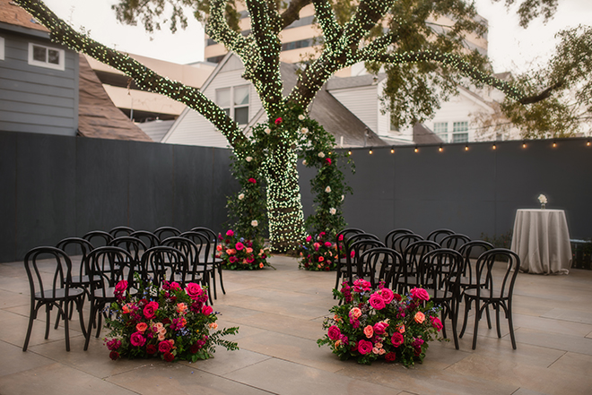Maroon and hot pink flowers detail the aisle and floral arch in the courtyard at Horizon on Sunset. 