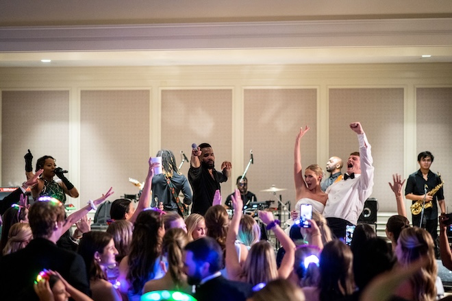 The bride and groom cheer on the stage while their wedding band performs on the stage at their wedding reception. 
