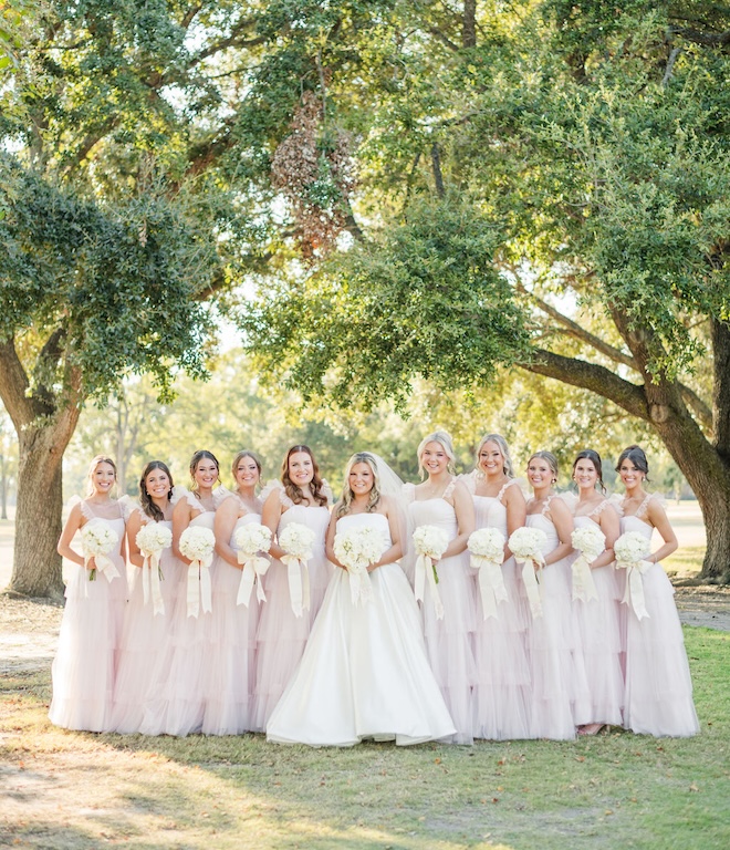The bridesmaids wear pink dresses as they hold their bouquets surrounding the bride outside at the Pine Forest Country Club. 
