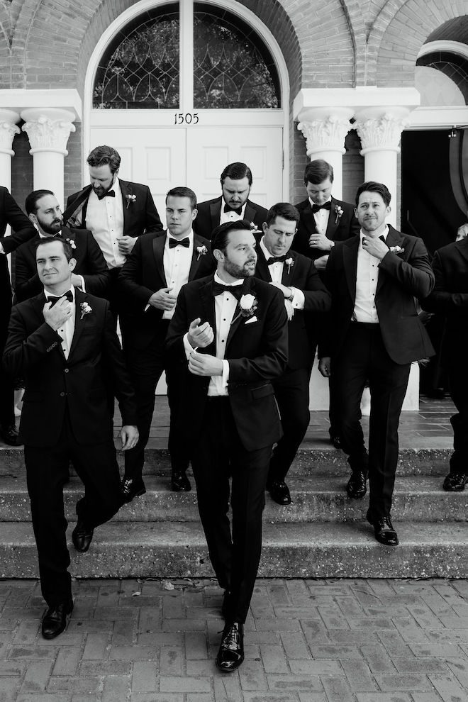 black and white photo of the groomsmen outside of the church fixing their cufflinks and ties.