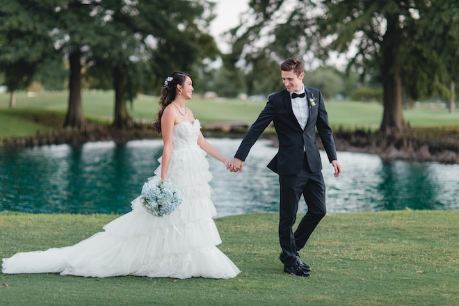 A bride and groom holding hands walking across the golf course of Pine Forest Country Club. 