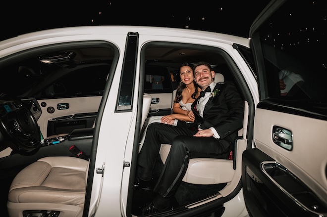 The bride and groom smile as they ride off in their white wedding day luxury getaway car. 