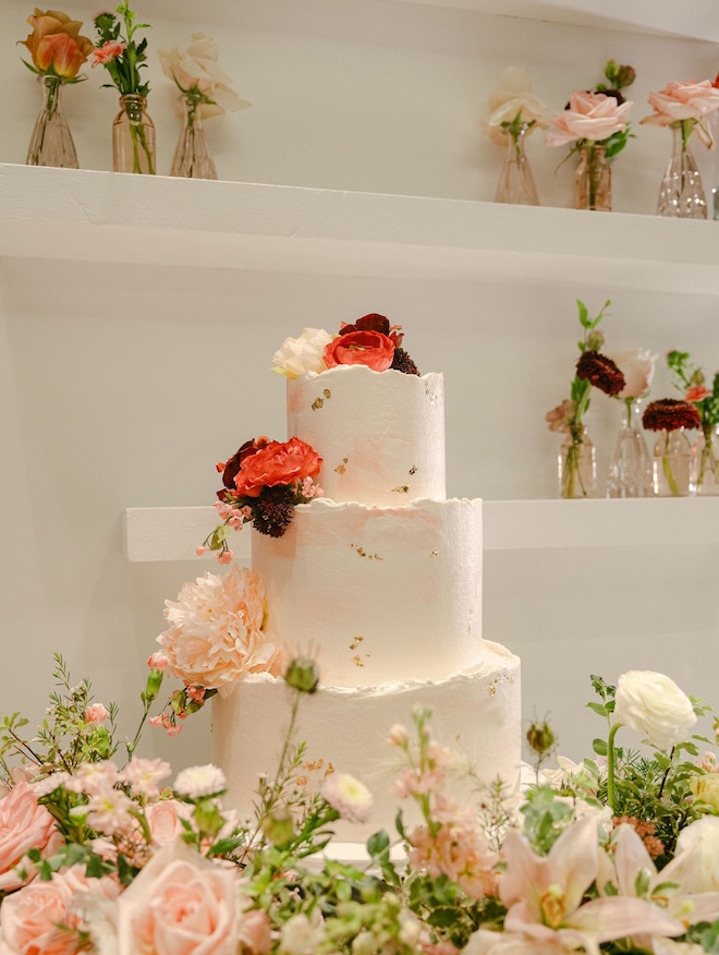 A pink marbled wedding cake is surrounded by an array of pink and white flowers. 