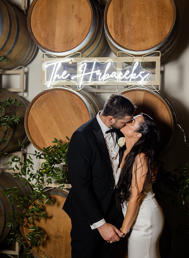 The bride and groom share a kiss under a neon sign that says "The Habaceks." 