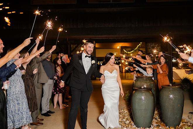 The bride and groom hold hands during their sparkler send-off from their emerald and gold wedding. 
