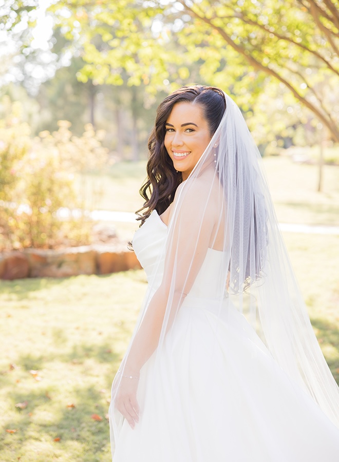 The bride looks over her left shoulder in her wedding dress and veil. 