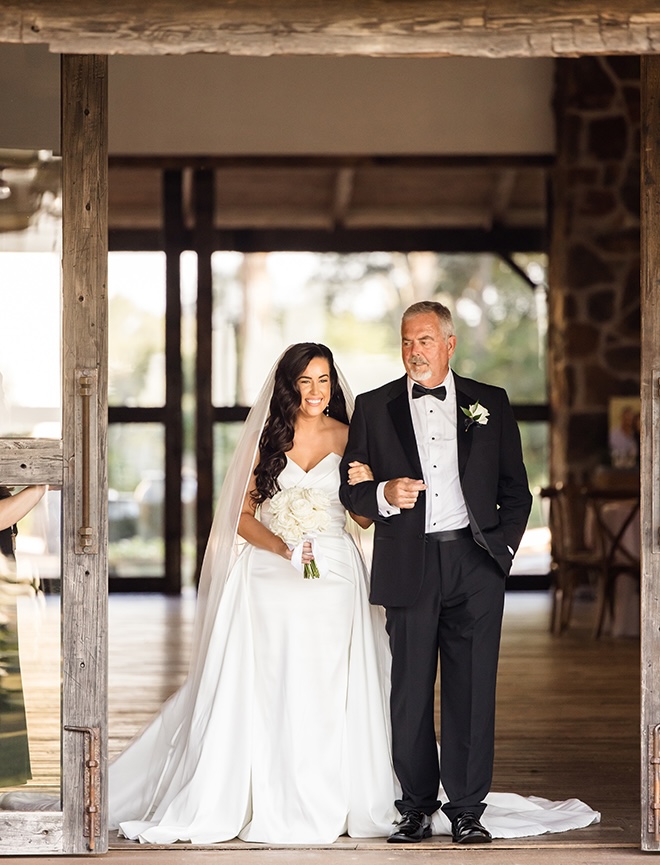 The father of the bride walks his daughter down the aisle for her outdoor wedding ceremony. 