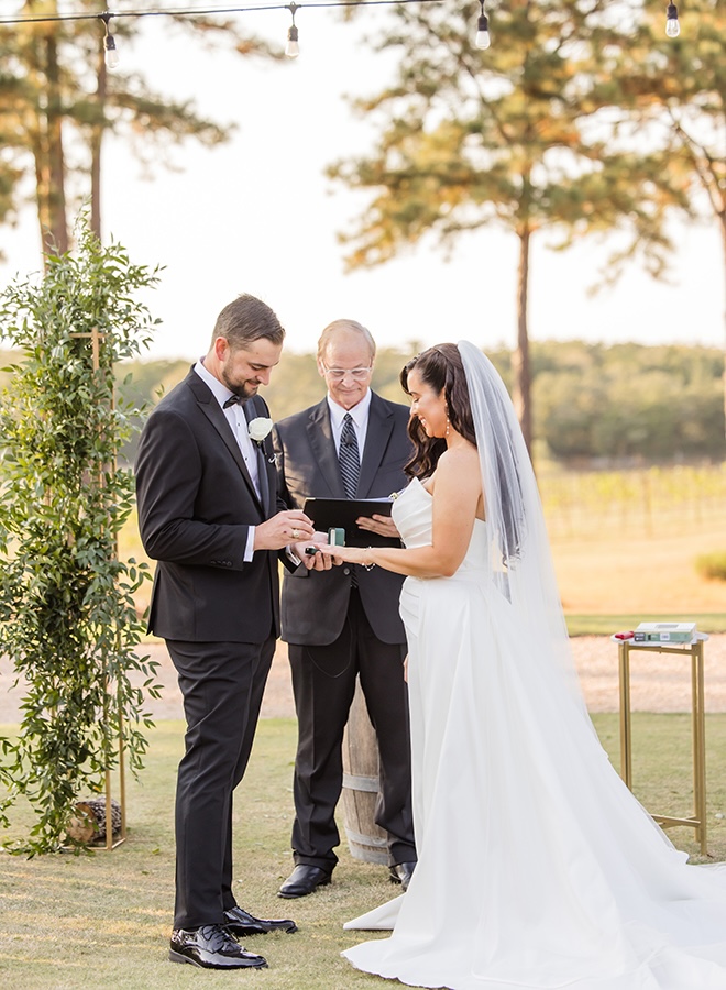 The groom puts the brides wedding band on her finger at their outdoor wedding ceremony. 