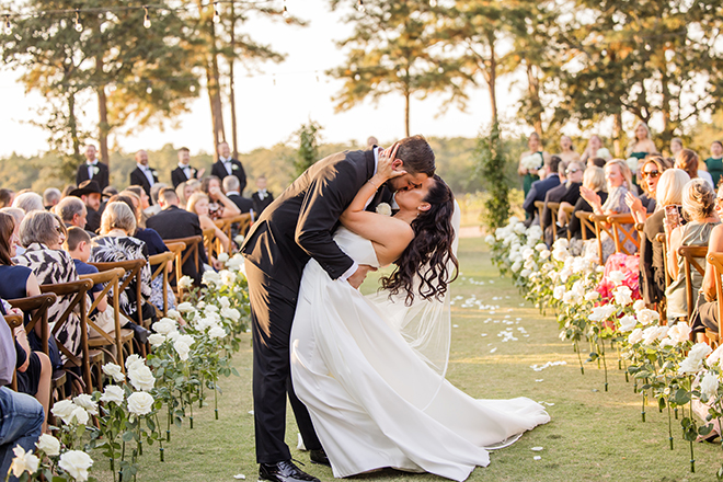 The bride and groom share a kiss in the middle of the aisle at their outdoor wedding ceremony. 