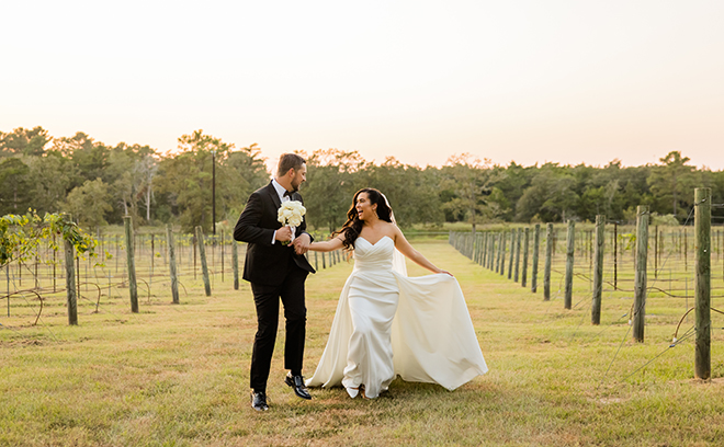 The bride and groom hold hands as they run down the vineyard. 