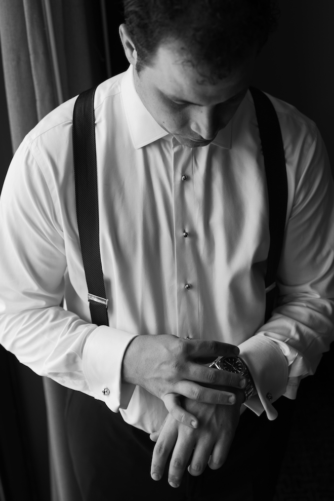 Black and white photo of the groom getting ready and looking down at his watch. 