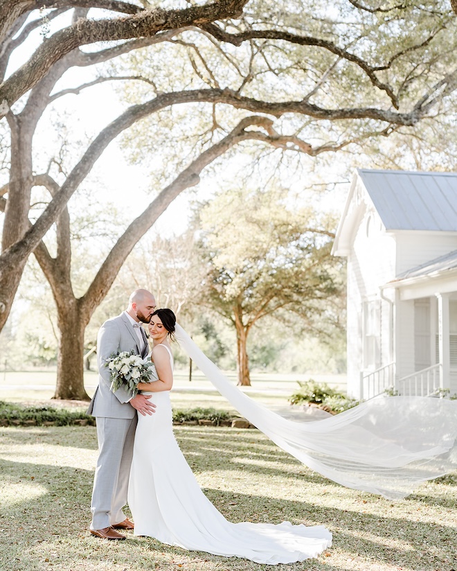 A groom kissing the bride's cheek underneath large trees at The Pattison House. 