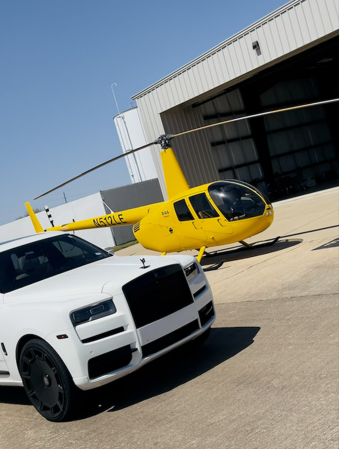 A yellow helicopter is next to a luxury white car by iExotic Car Rental & Chauffeur. 