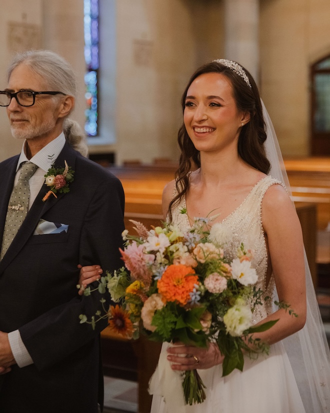 The bride and her father smiling while walking down the aisle. 