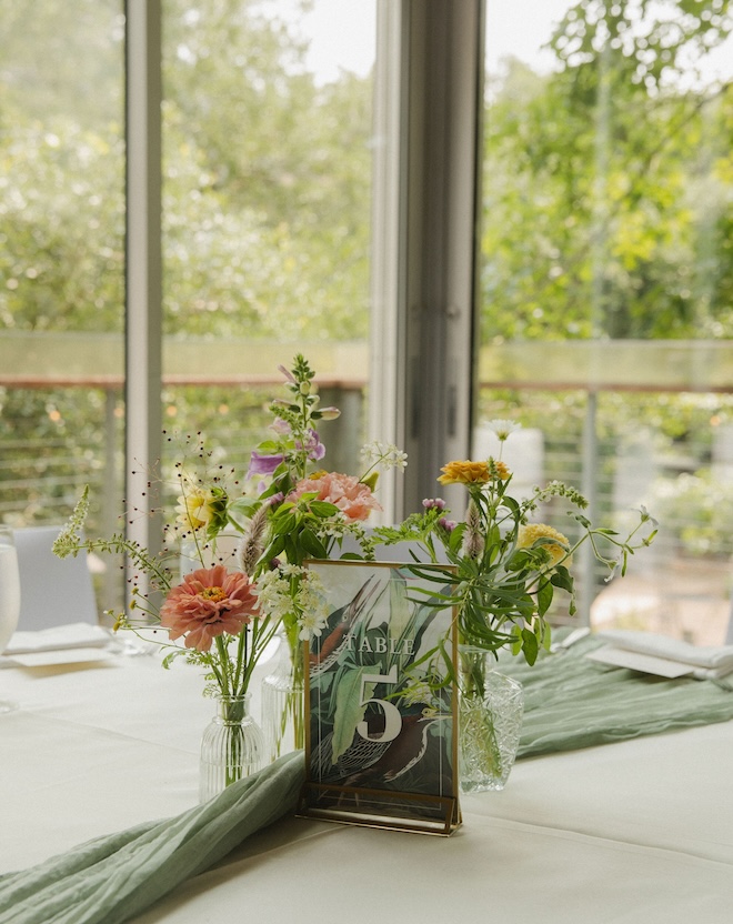 Multi-colored florals in bud vases and a printed tabe number with a bird on it for a New Orleans-Inspired wedding brunch.