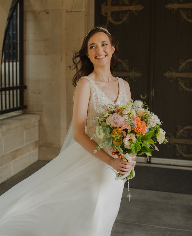 The bride smiling holding her bouquet while her dress flows in the wind. 