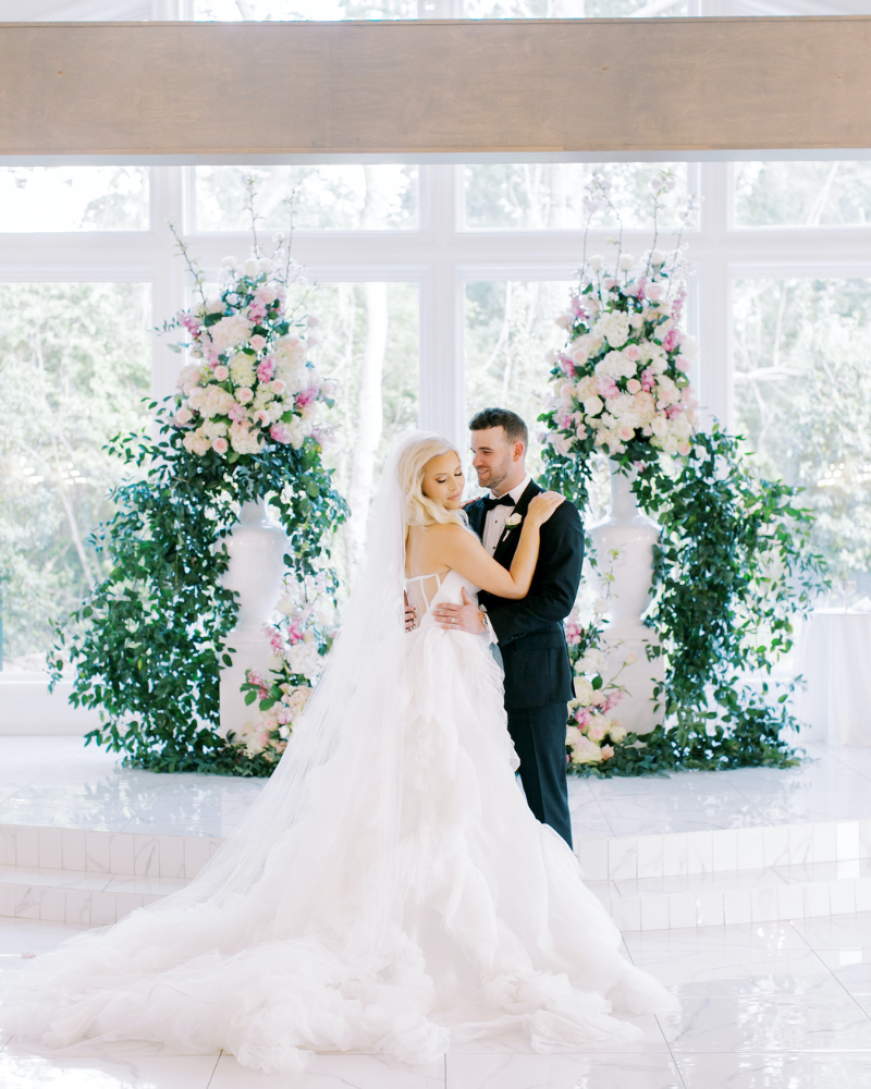Bride and groom holding each other at a pink and white floral adorned altar.
