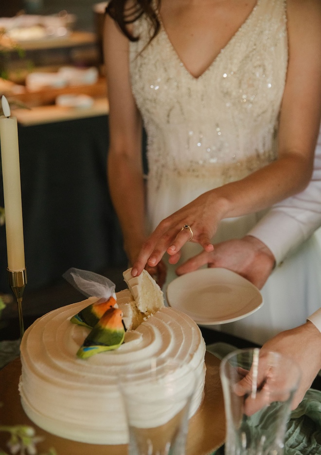 The bride and groom cutting their wedding cake that has two bird figurines on top. 