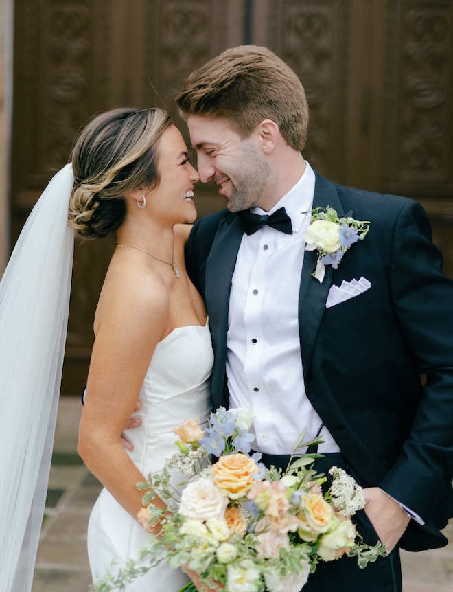 The bride and groom smiling at each other with the bride holding a pastel-colored bouquet. 