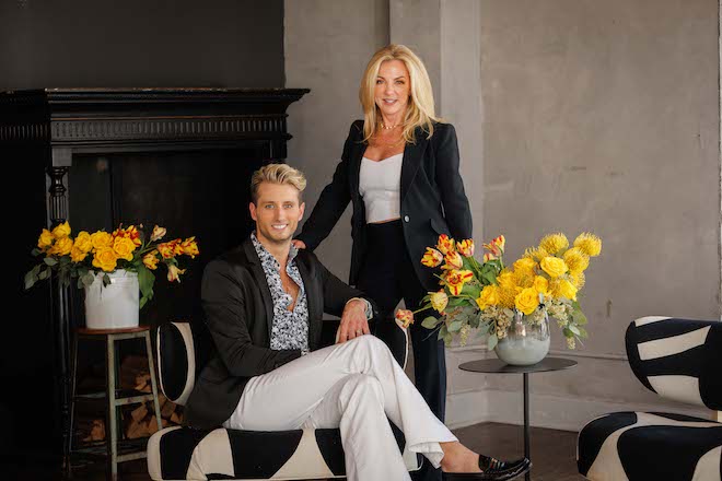 Owner Regina and events director Walker Chancey smiling and posing in between yellow flowers in a vase.