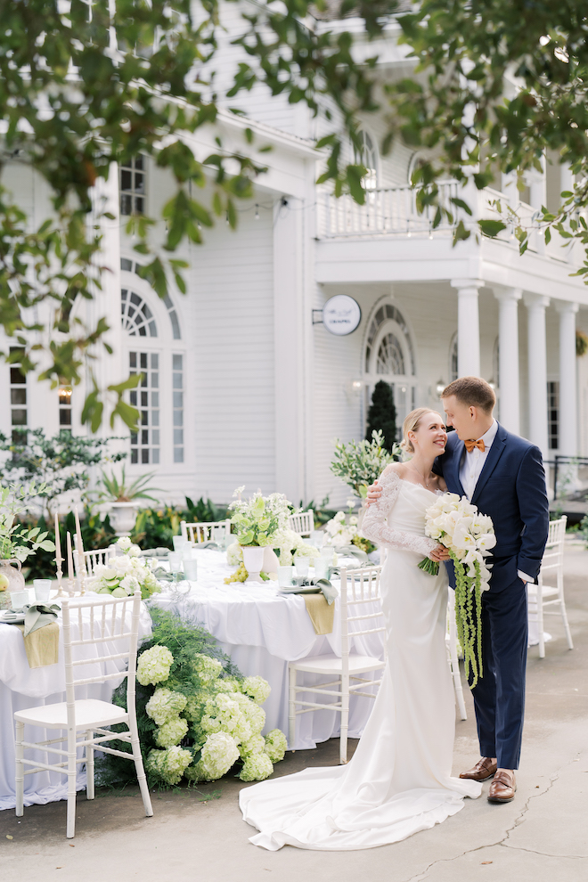 Bride and groom standing outside next to reception tables with a green and white floral theme.