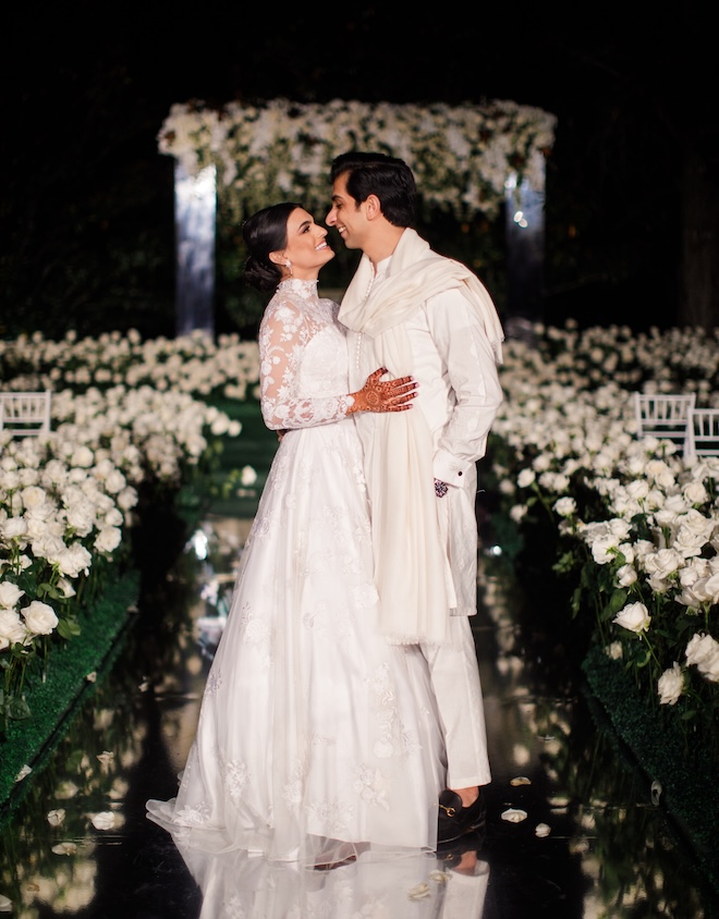 The bride and groom smile at each other as the stand in the middle of a mirrored aisle at their outdoor ceremony. 