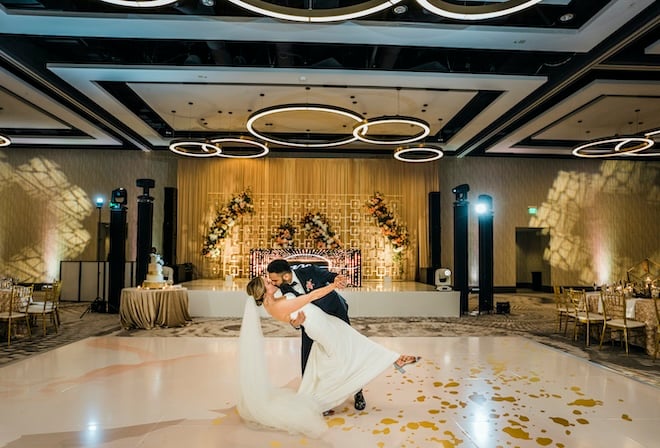 The groom dips the bride and gives her a kiss on a white and gold dance floor in the Marriott CityPlace's ballroom. 