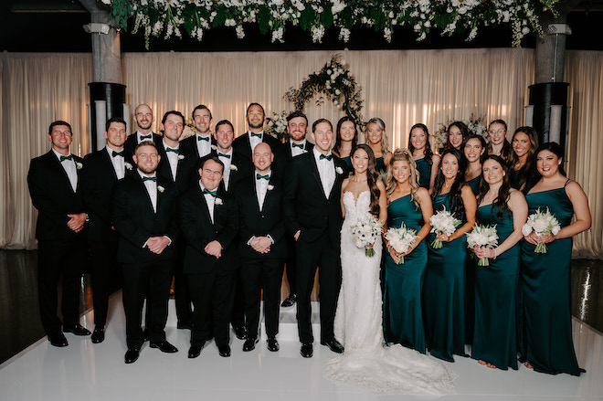 Newlywed couple with wedding party at the altar with bridesmaids in dark pine green.
