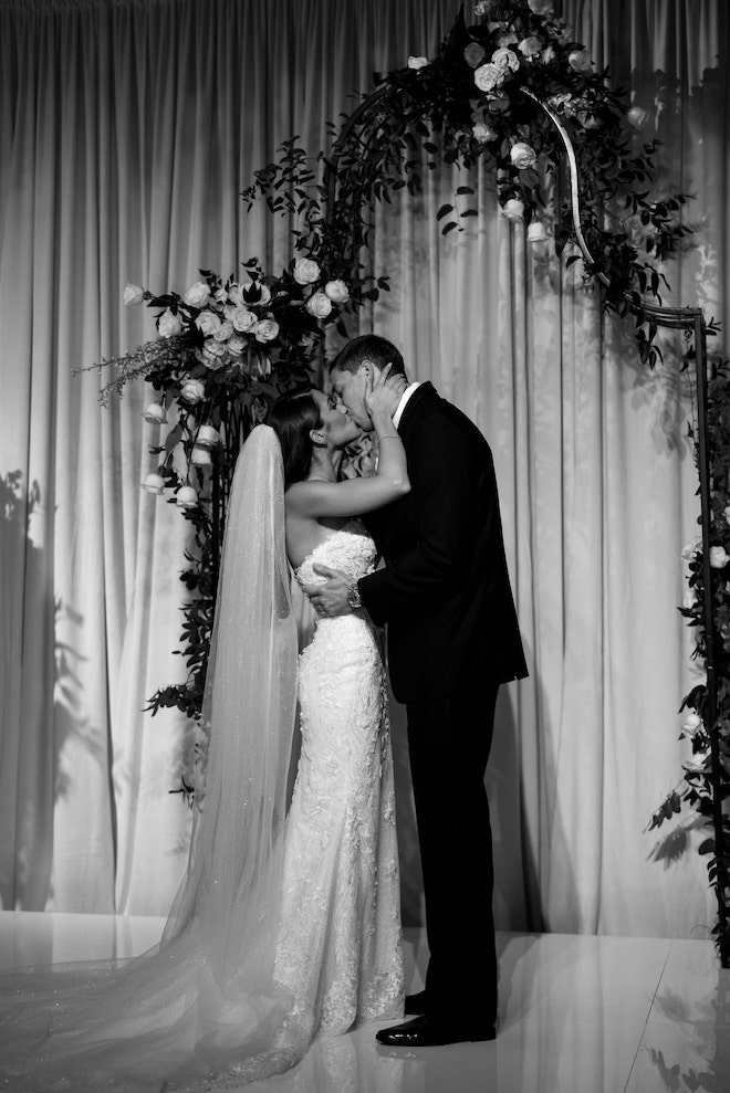 Black and white photo of bride and groom kissing at the altar.
