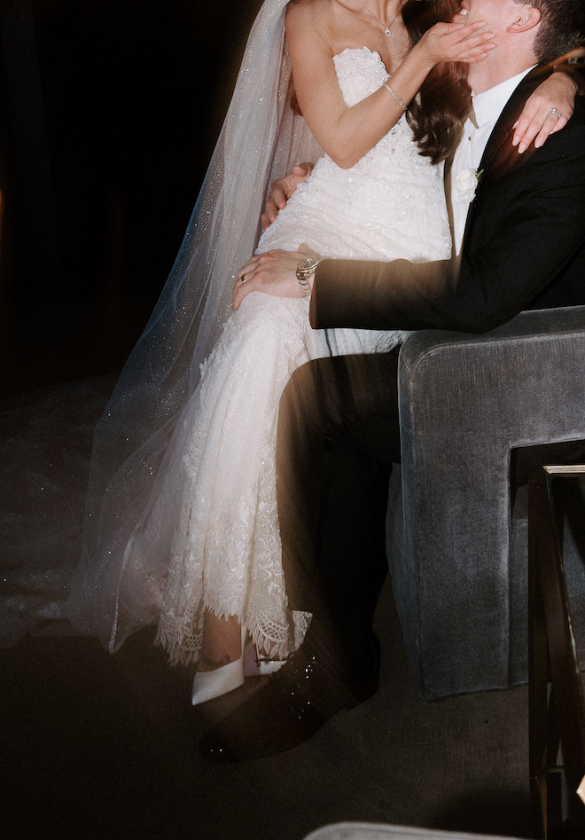 Bride sitting on groom's lap and holding his face while they smile at each other.