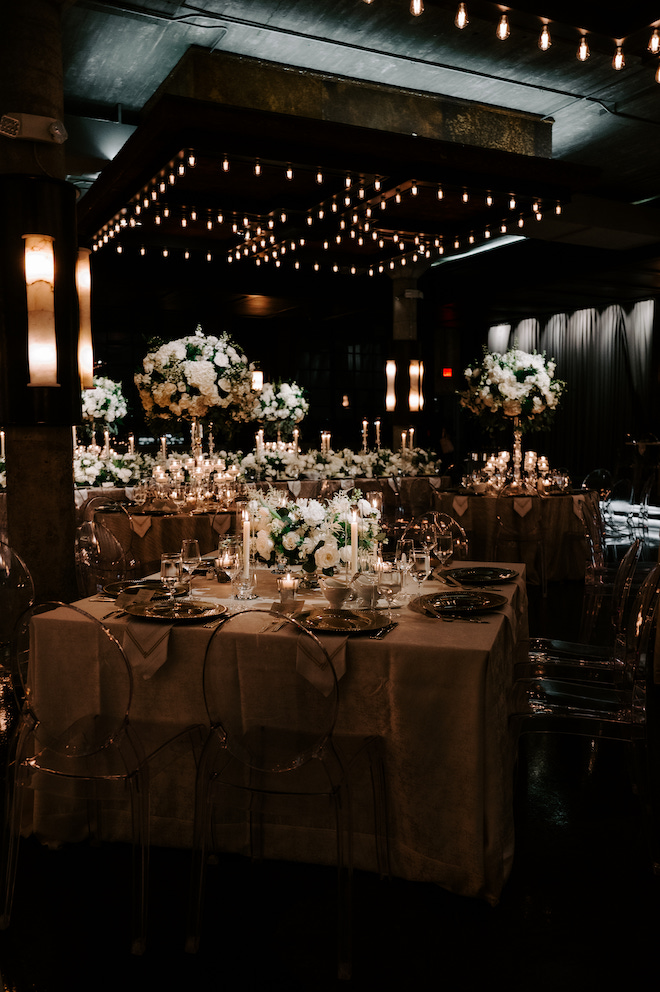 Reception table, with gold/nude table cloth, big green and white floral centerpieces, with white candles. 