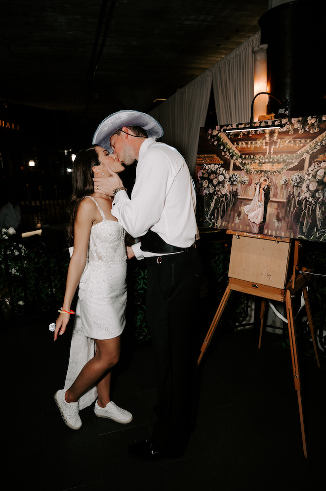 Bride and groom kissing in front of the live painter's painting of them kissing at the altar.