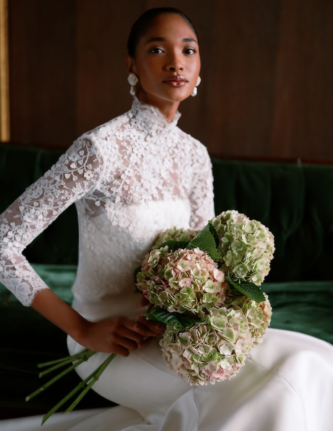 A bride holding hydrangeas and wearing a lace sleeved gown. 