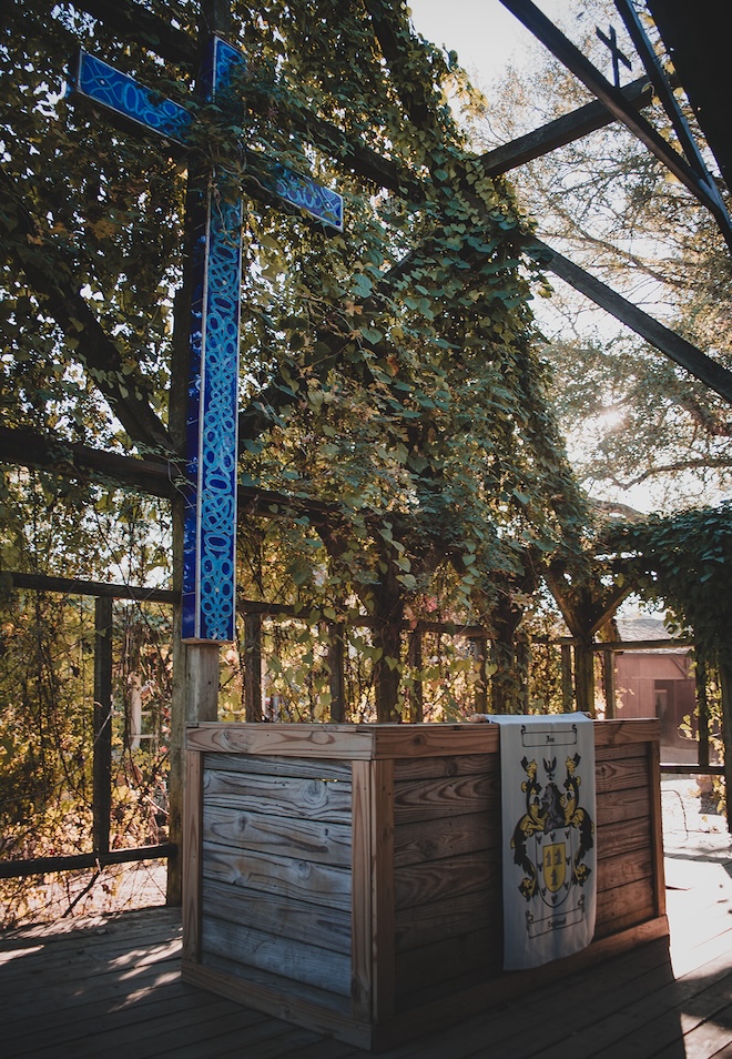 A blue cross hanging on the wall of the greenery-covered chapel.