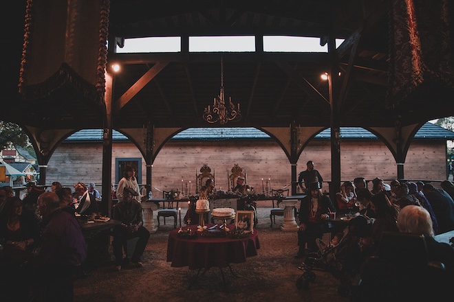 The bride and groom sitting at the reception with guests and their cakes. 