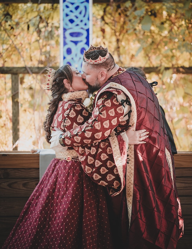Bride and groom in renaissance costumes kissing in the outdoor chapel. 