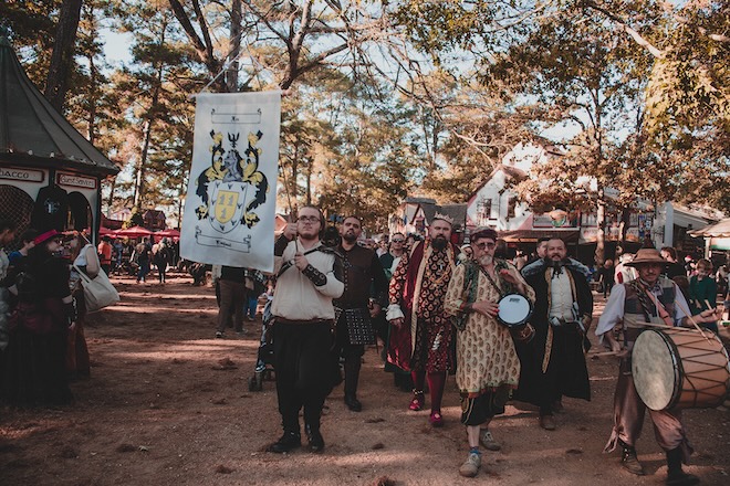 The groom and guests walking toward the chapel with men beating drums. 